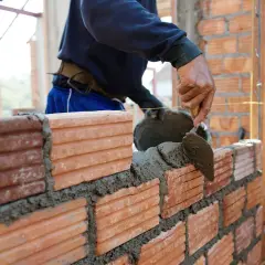 Murarz układa cegły, nakładając zaprawę kielnią. Sprawdza cenę za m2 robocizna murowania ścian.