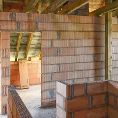 Budowa domu w toku: wznoszone są ściany z pustaków ceramicznych, widoczna ścianka kolankowa i drewniany strop.