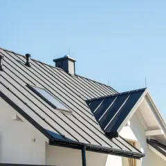 Nowoczesny dom z czarnym, metalowym dachem i kominami. Dachówka przypomina łuski świetlików, odbijając światło.