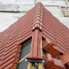 Nowy dach z brązowej dachówki. Widoczne miejsce przecięcia dwóch połaci dachowych, z elementami wentylacyjnymi i zapasem dachówek.
