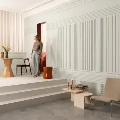 Elegancka kobieta wchodzi do salonu z nowoczesną lamperią. Wnętrze zdobią minimalistyczne meble i subtelne dekoracje.