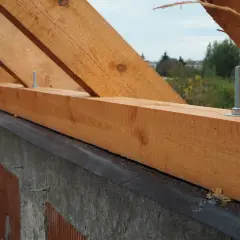 Drewniana murłata na betonowym wieńcu, przygotowana do montażu więźby dachowej. Widać śruby mocujące.