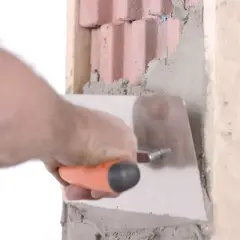 Dłoń z kielnią wygładza tynk wokół ceglanej framugi.