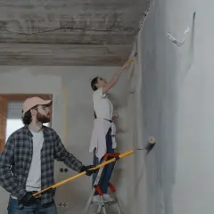 Para i córka malują ściany. Ona na drabinie, on z wałkiem w ręku.