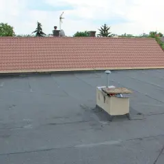 Płaski dach z papy, komin i fragmenty attyki z dachówką.
