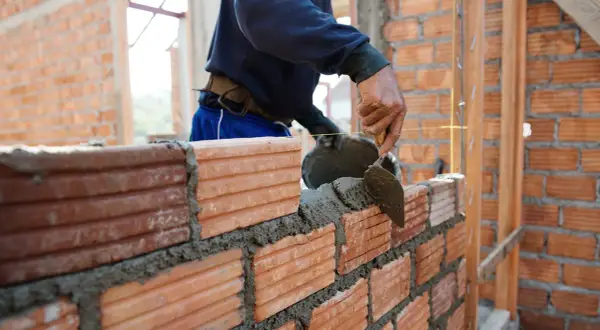 Murarz układa cegły, nakładając zaprawę kielnią. Sprawdza cenę za m2 robocizna murowania ścian.