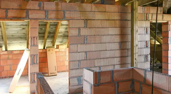Budowa domu w toku: wznoszone są ściany z pustaków ceramicznych, widoczna ścianka kolankowa i drewniany strop.