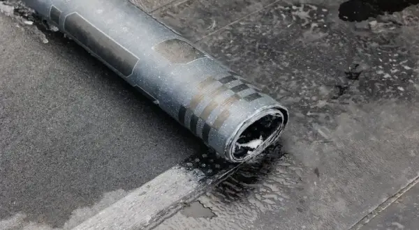 Zrolowana papa na zimno, z widocznymi czarnymi pasami i kratką, leży na mokrej, ciemnej powierzchni.