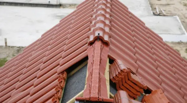 Nowy dach z brązowej dachówki. Widoczne miejsce przecięcia dwóch połaci dachowych, z elementami wentylacyjnymi i zapasem dachówek.