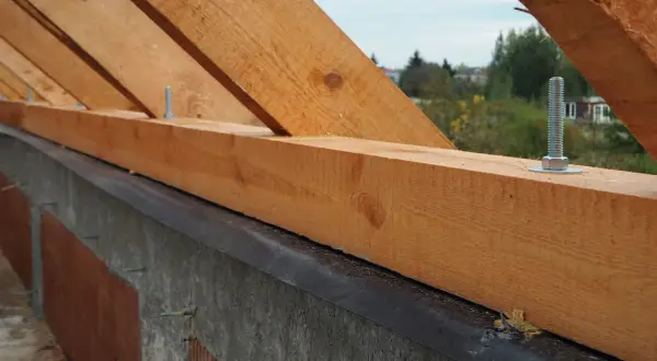 Drewniana murłata na betonowym wieńcu, przygotowana do montażu więźby dachowej. Widać śruby mocujące.