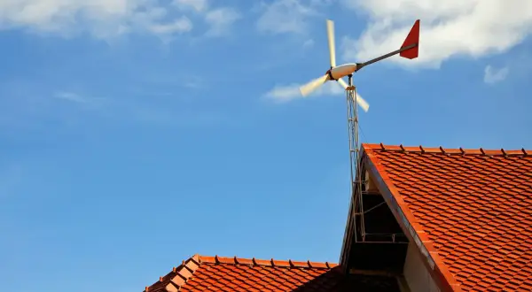 Mała przydomowa elektrownia wiatrowa na tle błękitnego nieba z chmurami, zamontowana na dachu.