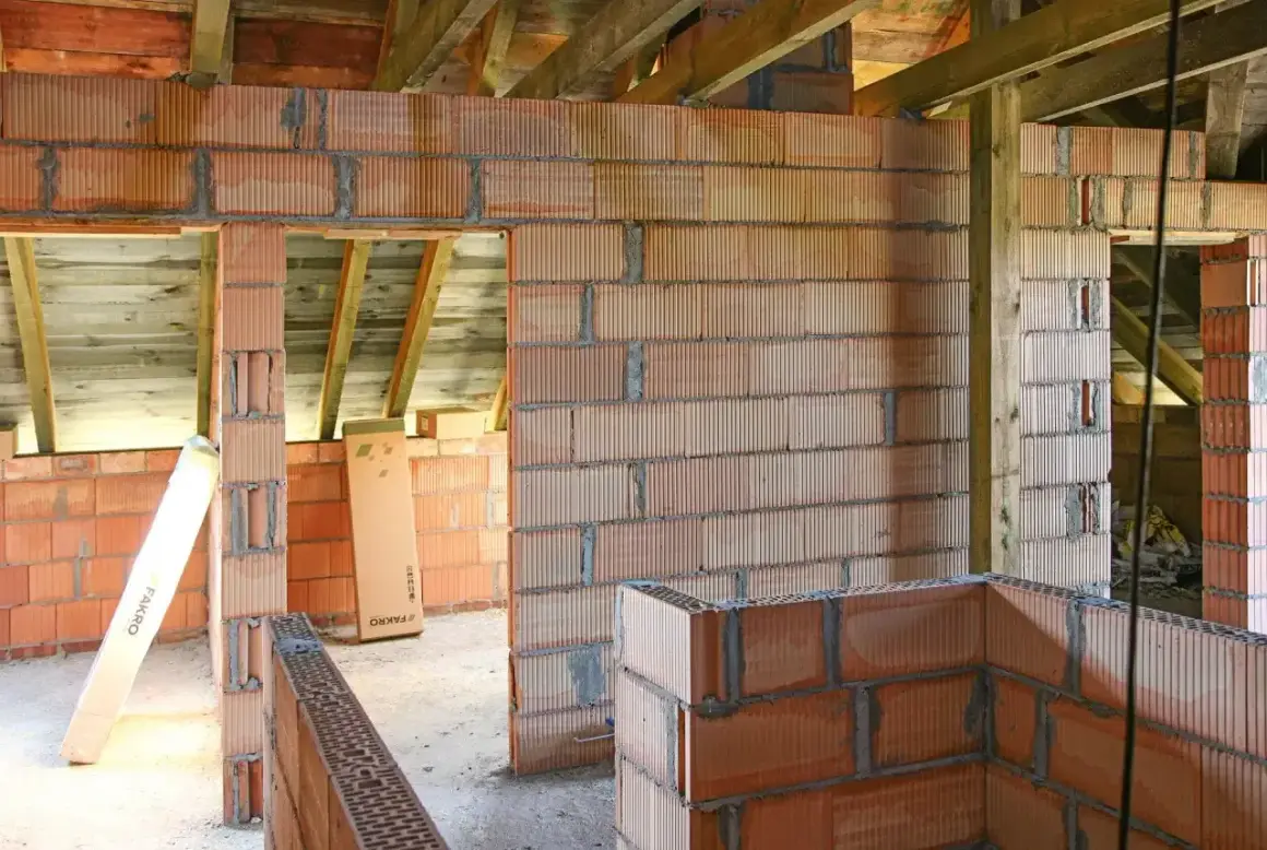 Budowa domu w toku: wznoszone są ściany z pustaków ceramicznych, widoczna ścianka kolankowa i drewniany strop.