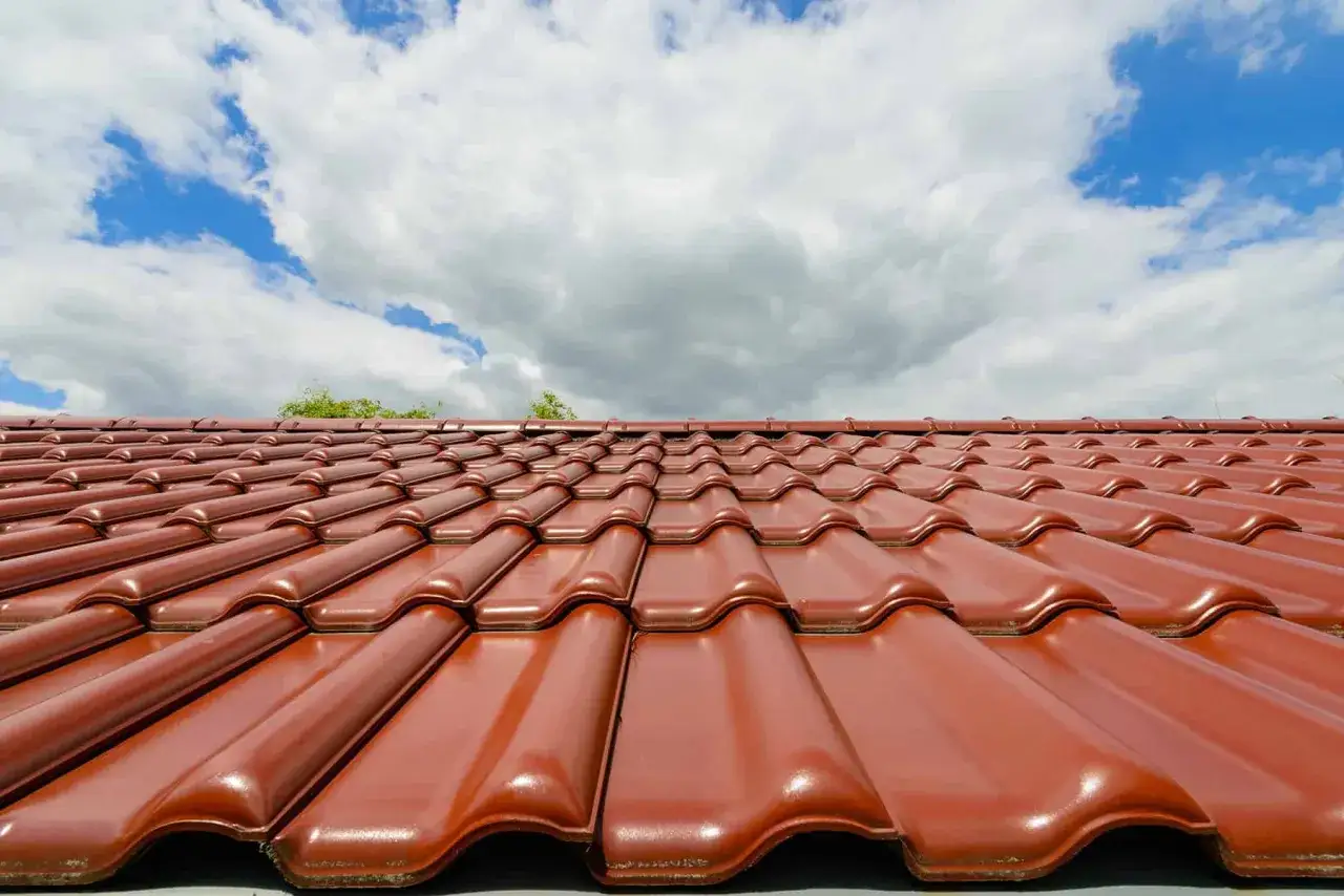 Czerwona dachówka ceramiczna błyszcząca pod błękitnym niebem. Sprawdź aktualną dachówka ceramiczna cena za m2.