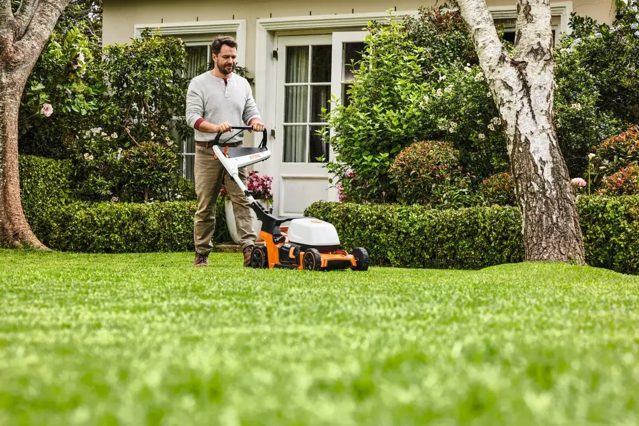 Mężczyzna z kosiarką STIHL wykonuje mulczowanie trawy w pięknym ogrodzie.