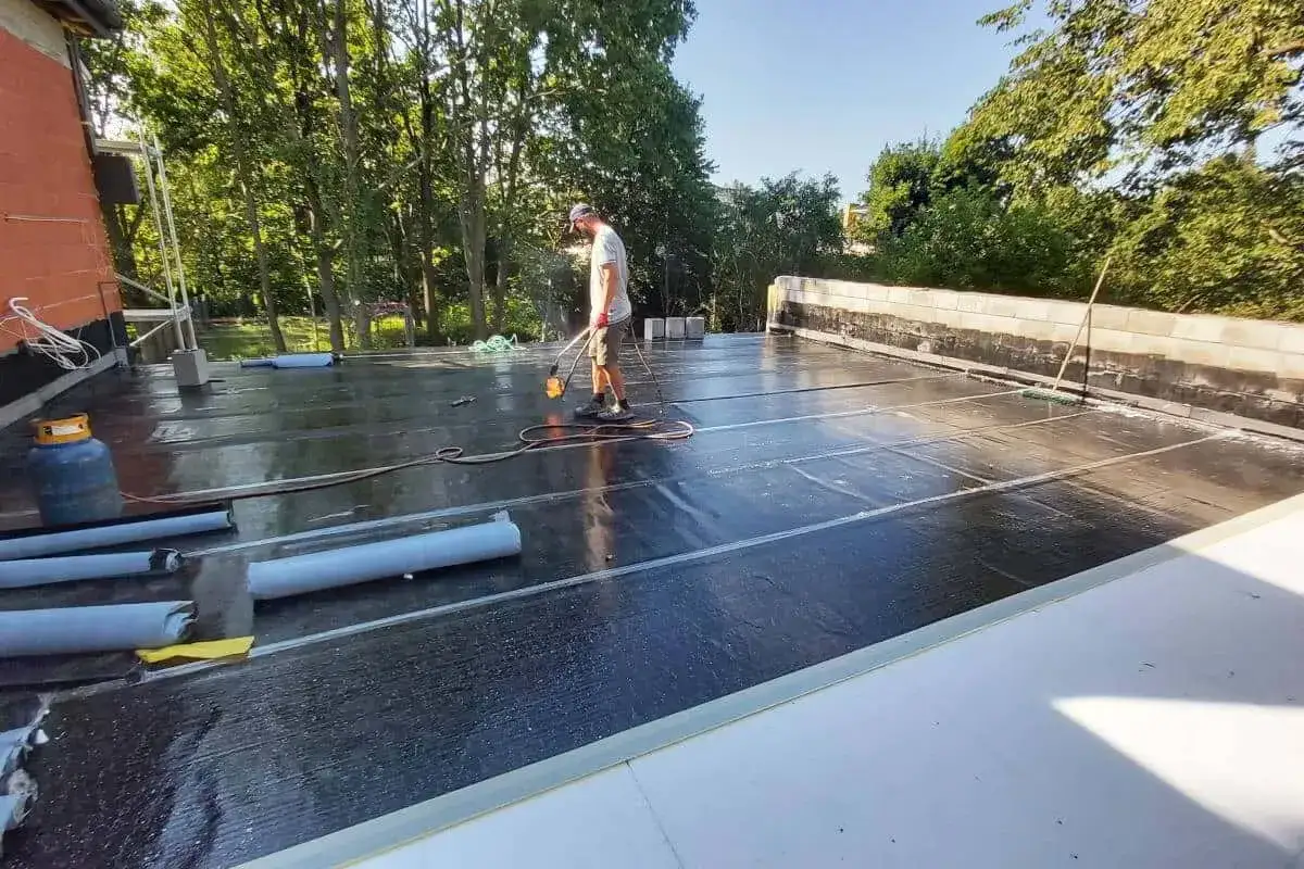 Pracownik wykonuje hydroizolację tarasu nad garażem, używając palnika do papy.