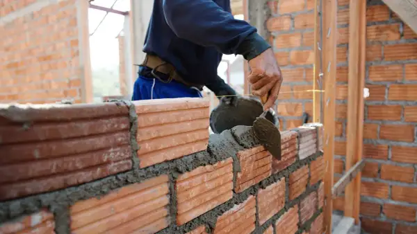 Murarz układa cegły, nakładając zaprawę kielnią. Sprawdza cenę za m2 robocizna murowania ścian.