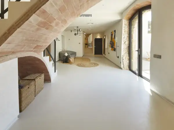 Nowoczesny hol z łukiem z cegły, gdzie **mikrocement na płytki** tworzy gładką, jednolitą podłogę. Wnętrze zdobią plecione kosze i abstrakcyjne obrazy.