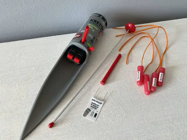Pułapka na krety z mechanizmem spustowym i kilkoma czerwonymi "petardami" z pomarańczowymi linkami.