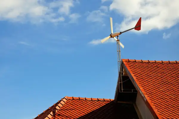Mała przydomowa elektrownia wiatrowa na tle błękitnego nieba z chmurami, zamontowana na dachu.