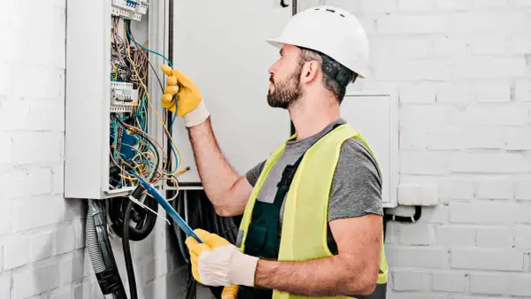 Elektryk w kasku i kamizelce odblaskowej pracuje przy skrzynce z przewodami. Dokładna wycena koszt instalacji elektrycznej.