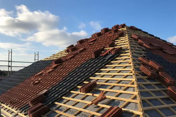 Układanie dachówki na drewnianej konstrukcji. Widać łaty i kontrłaty rozstaw, przygotowane pod pokrycie.