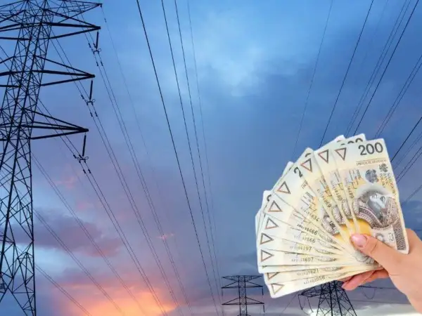 Dłoń trzyma banknoty 200 zł na tle linii energetycznych. Zastanawiasz się, ile kosztuje 1 kWh PGE?