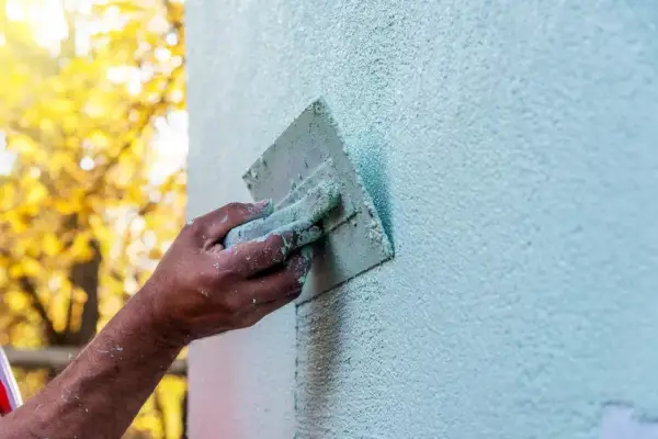 Dłoń z kielnią nakłada tynk na ścianę, tworząc fakturę. Różne rodzaje tynków wewnętrznych dają ciekawe efekty.